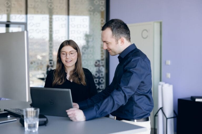 zwei SOLTIC-Mitarbeitende blicken lächelnd auf ein Laptop